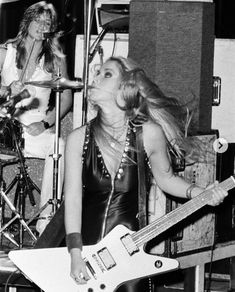 two women in leather outfits playing guitars and singing into microphones while another woman stands behind them