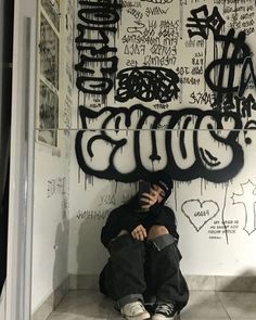 a man sitting on the ground in front of a wall covered with graffiti