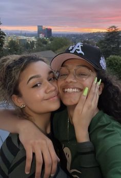 two young women hugging each other in front of a sunset