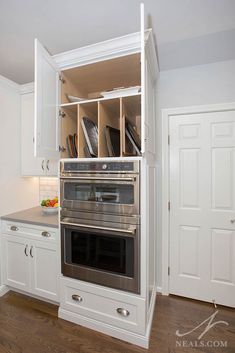 an oven built into the wall in a kitchen with white cabinets and wood flooring