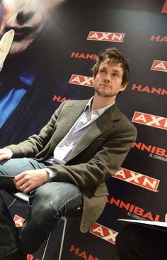 a man sitting on top of a chair in front of a wall with an advertisement