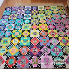 a colorful quilt is laying on the floor in front of a wooden table with black polka dots