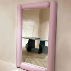 a pink mirror sitting on top of a wooden floor next to a white table and chair