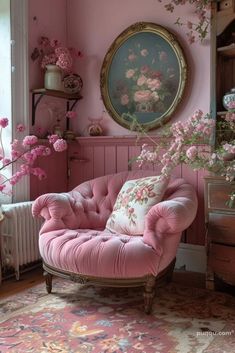 a pink chair in front of a window with flowers on it and a mirror behind it