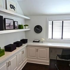 an office with white cabinets and black accessories on the shelves, along with a clock