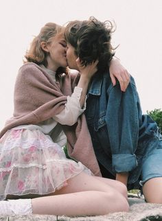 two women sitting on the ground kissing each other