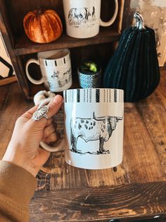 a person holding a coffee mug in front of a shelf with pumpkins and other items