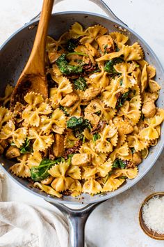 a skillet filled with pasta and spinach on top of a white counter next to a wooden spoon