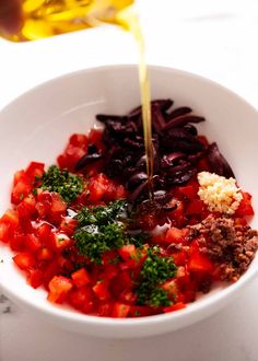 someone pouring dressing into a white bowl filled with red and green vegetables, including broccoli