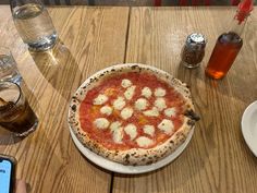 a pizza sitting on top of a white plate next to a cup of coffee and a cell phone