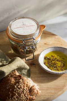 a wooden plate topped with bread next to a bowl of olive oil and a jar of seasoning