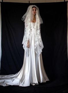 a woman in a white wedding gown and veil standing next to a black backdrop with the back of her dress pulled up