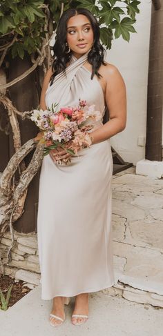 a woman standing in front of a tree holding a bouquet