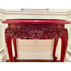 a red console table with flowers on the top and bottom, sitting in front of a white wall