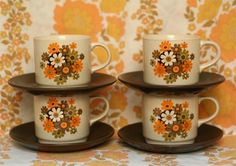 four coffee cups with orange and white flowers on them sitting on a brown saucer