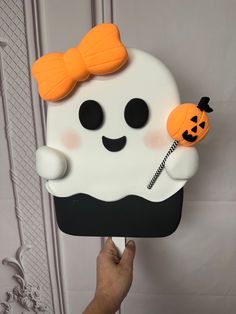 a person holding up a cake shaped like a ghost with a pumpkin on its nose