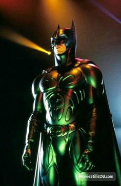 a man in a batman costume standing next to a stage light with his hands on his hips