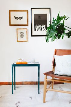 a chair and table in a room with pictures on the wall above it, along with a potted plant