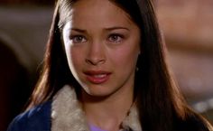 a close up of a person with long hair and wearing a blue jacket, looking at the camera