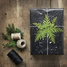 an image of a gift wrapped in black paper with a green tree on it and sprigs of thread next to it