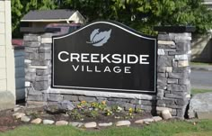 a black and white sign that reads creekside village in front of a house with flowers