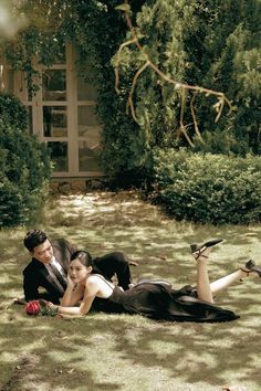 a man and woman laying on the ground next to each other in front of some bushes