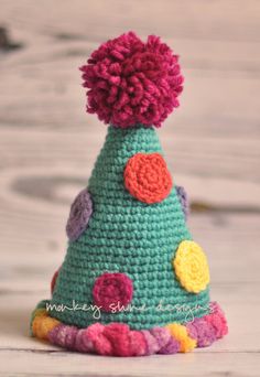 a crocheted party hat with pom - poms on the top, sitting on a wooden surface