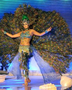 a woman in a costume with peacock feathers on her head and arms, walking down a runway