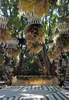 an outdoor wedding setup with white chairs and greenery hanging from the ceiling, surrounded by tall trees