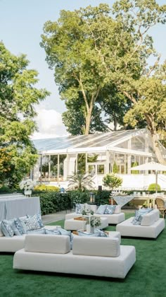 an outdoor seating area with white couches and pillows on the grass in front of a house