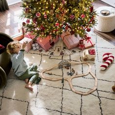 a small child playing with a train set in front of a christmas tree on the floor