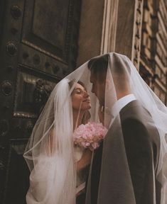 a bride and groom standing in front of a church door with their veil blowing in the wind