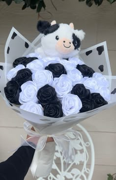 a person holding a bouquet of roses with a stuffed animal in the center and black and white flowers