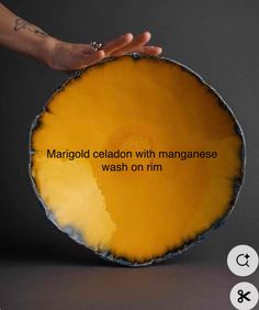 a person holding up a yellow plate with words on it that read marjold celadon with mangoese wash on rm