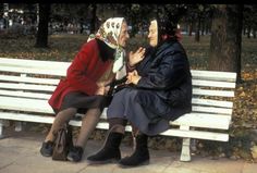 two women sitting on a white bench in the park, one is talking to the other