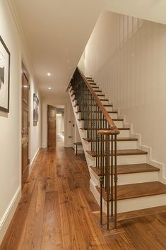 an empty hallway with wooden floors and stairs leading up to the second floor, along with framed pictures on the wall