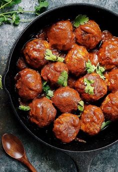 a person holding a spoon in a skillet filled with meatballs and garnished with cilantro