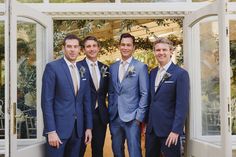 three men in suits are posing for a picture outside the door to their wedding venue