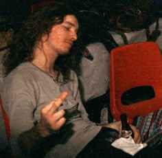 a man with long hair sitting in a red chair and holding a bottle next to him