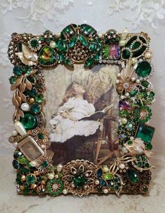 an ornate frame is adorned with green and gold jewels, pearls, and glass beads