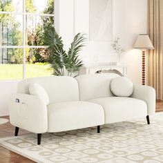 a white couch sitting on top of a wooden floor next to a lamp and window