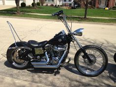 a black motorcycle parked on the side of a road next to a tree and house