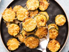 cooked zucchini on a black plate with a silver serving spoon in the middle