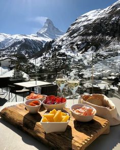 two bowls of food on a wooden table with mountains in the background and wine glasses