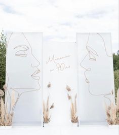 three white canvass with faces drawn on them in front of some trees and bushes