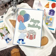 a birthday card with balloons, presents and other items on a tray next to it