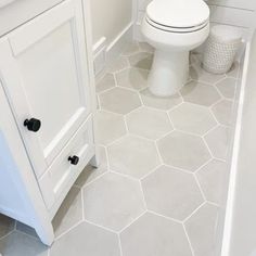 a white toilet sitting in a bathroom next to a sink and bathtub with hexagonal tiles on the floor