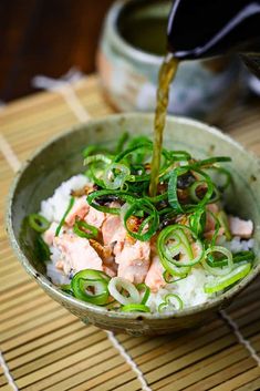 salmon and green onions are being poured into a bowl with rice on the table next to it