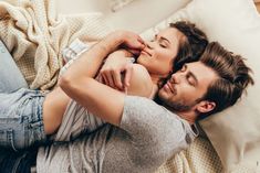 a man and woman laying in bed with their arms around each other, looking at the camera