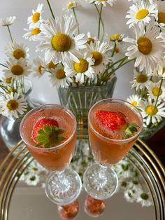 two wine glasses with strawberries in them on a table next to some daisies